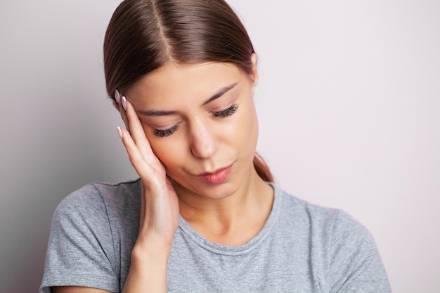 Una joven cansada siente dolor de cabeza y sostiene el lugar del dolor con las manos.