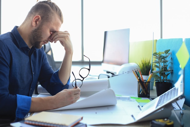 Joven cansado está trabajando con papeles mientras está sentado en la oficina.