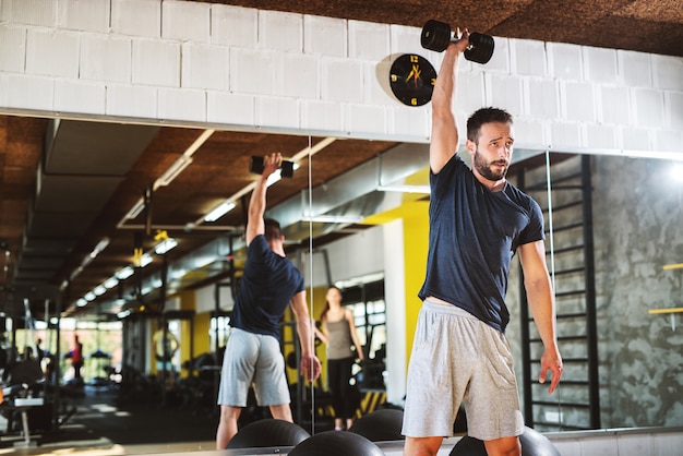 Foto joven cansado hombre fuerte levantando pesas en un gimnasio.