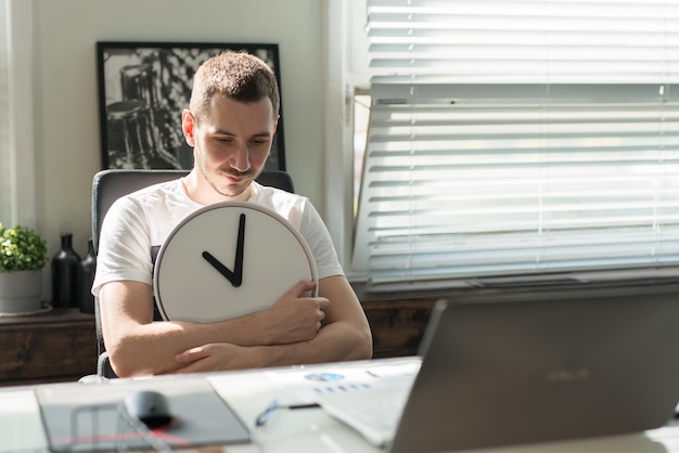 Foto el joven cansado se sienta triste en el escritorio y abraza el reloj