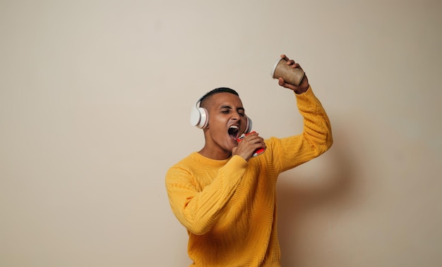 joven cantante escucha música con auriculares y micrófono móvil sosteniendo una taza de café