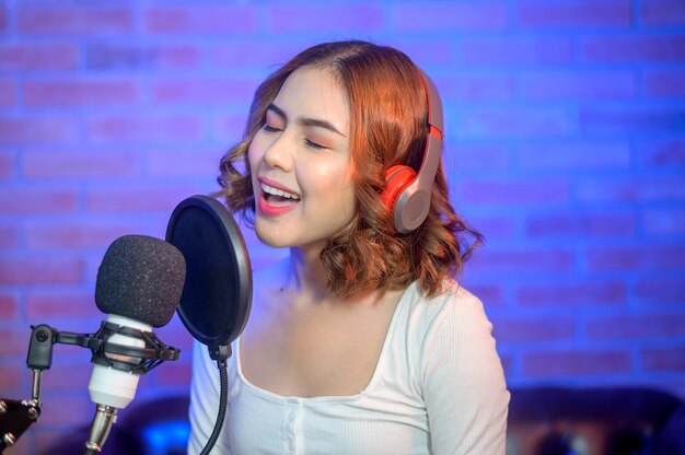 Una joven cantante sonriente con auriculares con micrófono mientras graba una canción en un estudio de música con luces de colores.