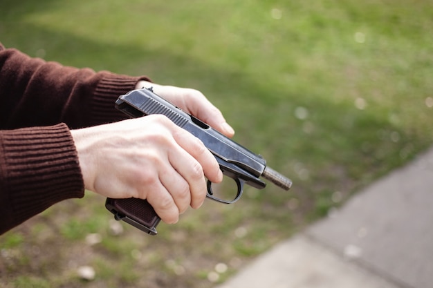 Un joven carga una pistola contra una hierba verde. Pistola de armas de fuego