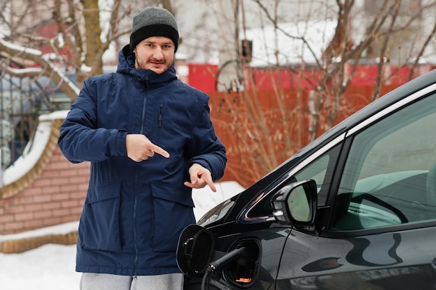 Joven cargando su coche eléctrico en invierno Concepto de transporte ecológico