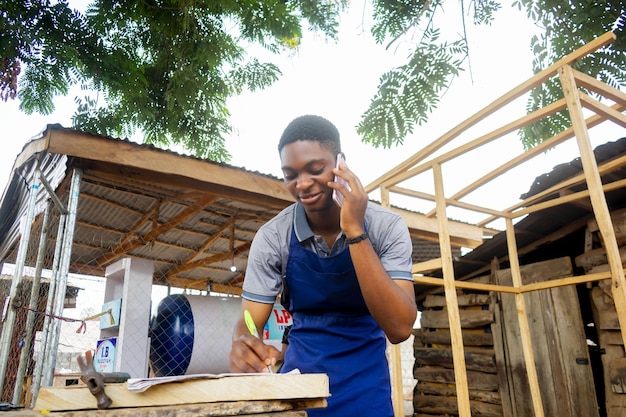 Foto joven carpintero africano de pie sosteniendo una llamada de trabajo