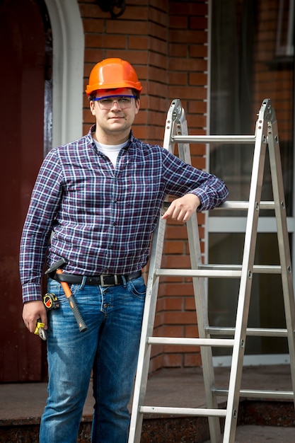 Joven carpintero en casco posando en escalera metálica