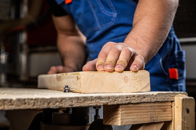 Un joven carpintero constructor iguala una barra de madera con una fresadora en el taller