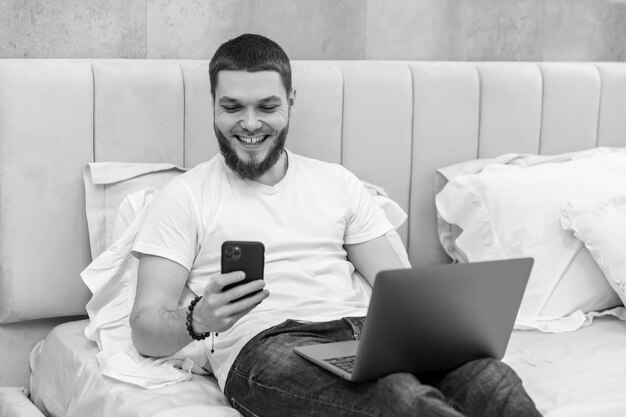 Joven en casa en el sofá con una laptop mirando el teléfono