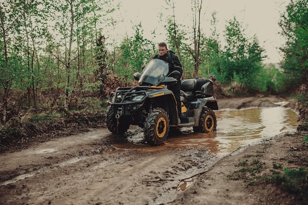 Un joven con un casco blanco recorre el bosque en un quad Hobby extremo Un viaje en ATV en el camino de troncos Quad Biking por el bosque