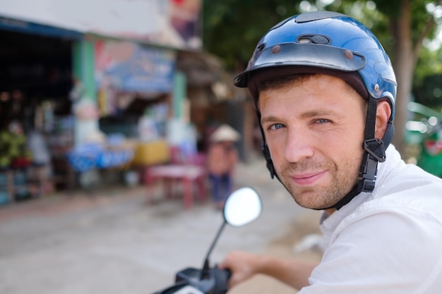 Un joven con casco se queda en una carretera de Asia mirando a la cámara