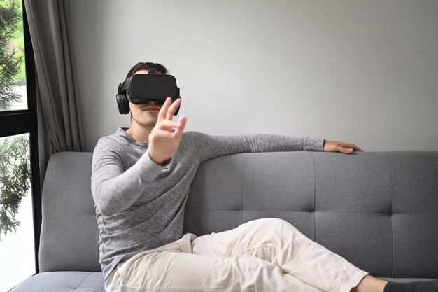 Joven con casco de realidad virtual y jugando videojuegos o viendo películas en casa