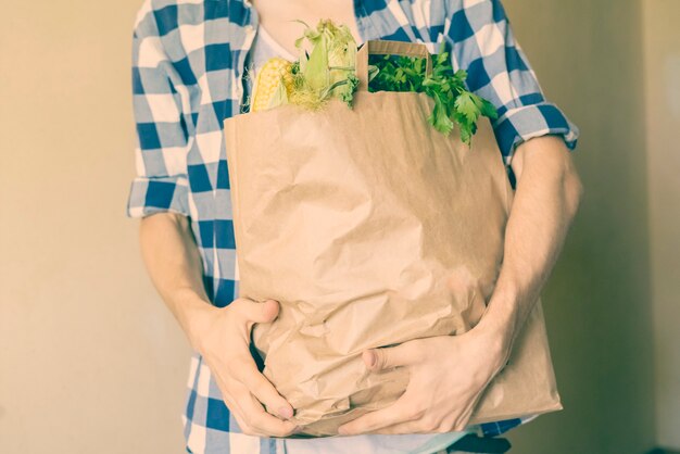 Un joven en casual llegó a casa de una tienda de alimentos y compró comestibles frescos en una bolsa de papel.