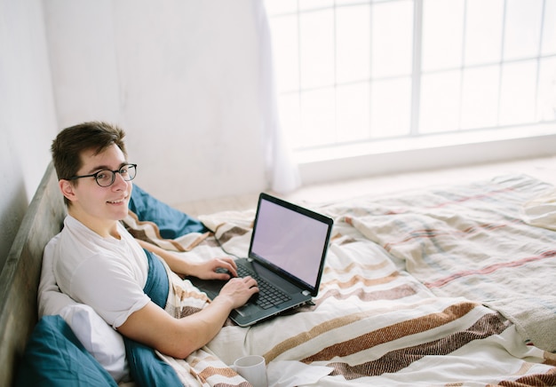 Joven casual usando laptop en la cama en casa