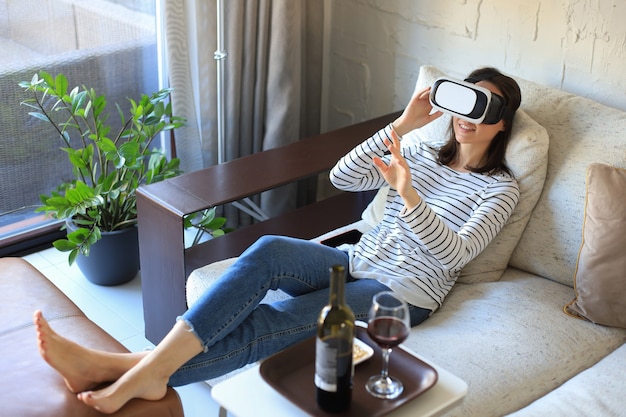 Joven casual vistiendo auriculares VR mientras descansa en el sofá en casa y mira a su alrededor.