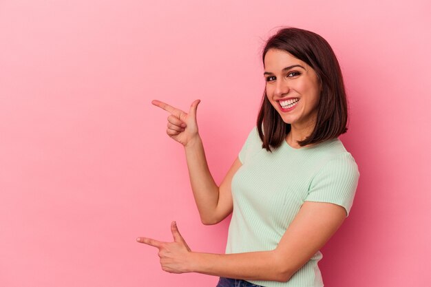Una joven caucásica aislada de fondo rosa emocionada señalando con los dedos índices.