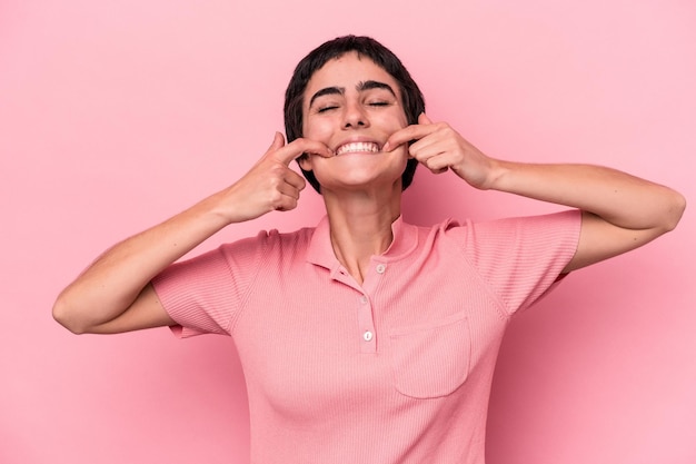 Foto una joven caucásica aislada de fondo rosa sonríe apuntando con el dedo a la boca