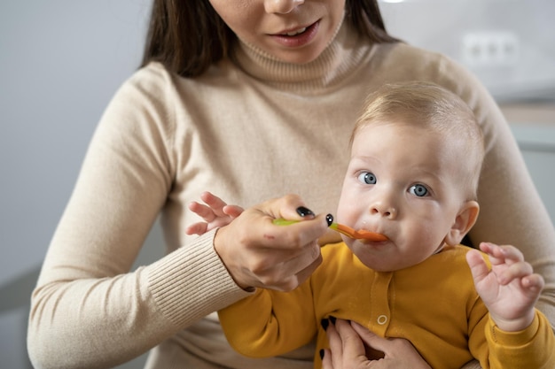 Foto una joven caucásica alimenta a su hijo con gachas de una cuchara en la cocina. una mujer con su hijo está sentada a la mesa. copie el espacio.