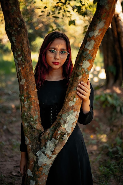 Joven caucásica de cabello oscuro con rayas rojas vestidas de negro con cinturón de corsé y gafas posando para una sesión de belleza femenina