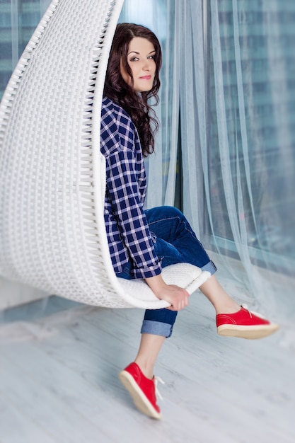 Joven caucásica con cabello rizado oscuro con una camisa a cuadros azul, jeans y zapatillas rojas.