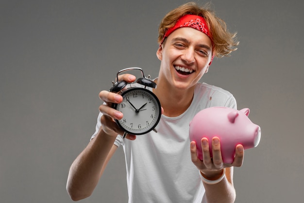 Joven caucásica, camiseta blanca con caja de dinero de cerdo rosa en la pared gris