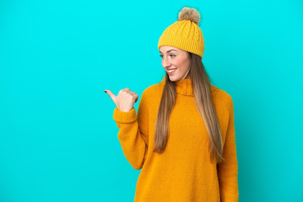 Joven caucásica con chaqueta de invierno aislada de fondo azul apuntando hacia un lado para presentar un producto