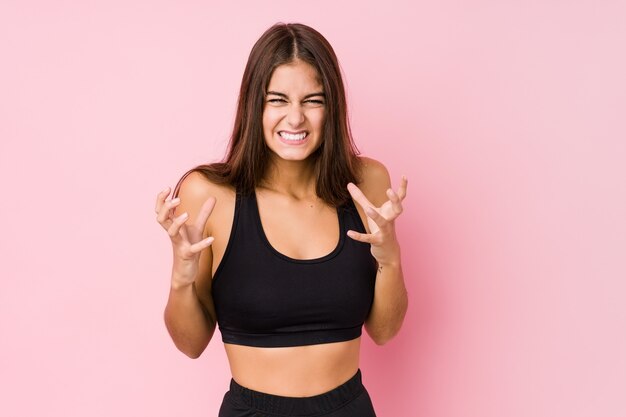 Joven caucásica fitness mujer haciendo deporte molesto gritando con las manos tensas.