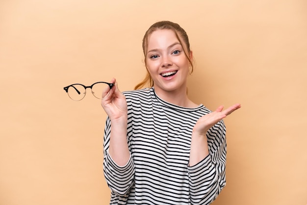 Joven caucásica con gafas aisladas de fondo beige con expresión facial sorprendida