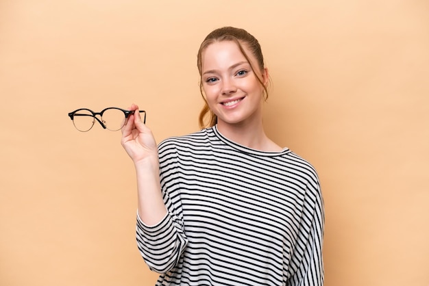 Joven caucásica con gafas aisladas de fondo beige sonriendo mucho