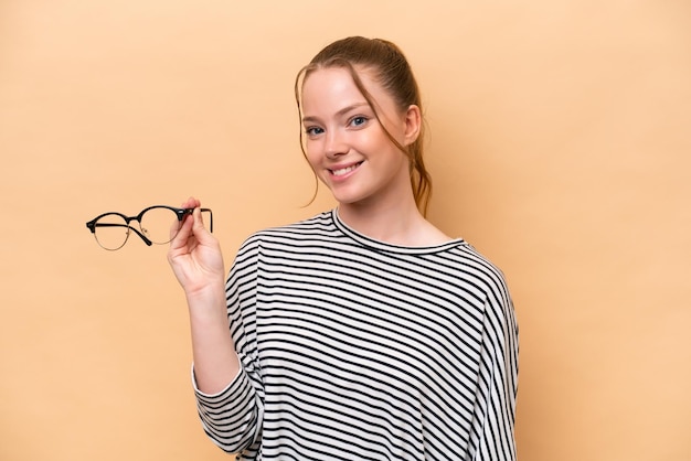 Joven caucásica con gafas aisladas de fondo beige sonriendo mucho