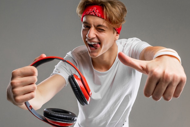 Joven caucásica en gafas de sol rojas, camiseta blanca escucha música con grandes auriculares rojos en la pared gris