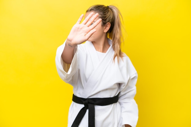 Joven caucásica haciendo karate aislada de fondo amarillo haciendo un gesto de parada y decepcionada