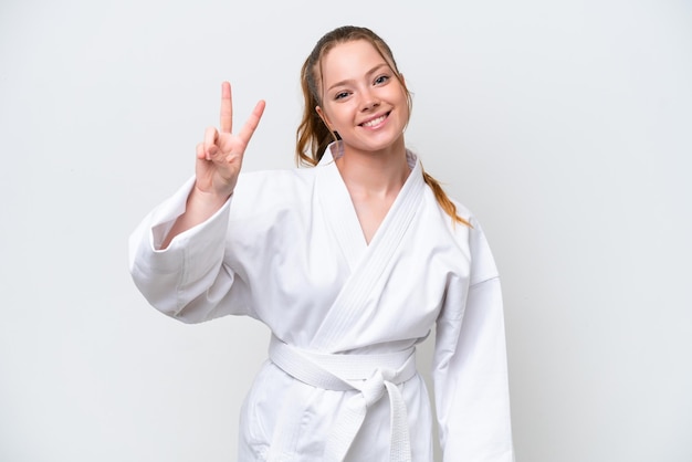 Joven caucásica haciendo karate aislada de fondo blanco sonriendo y mostrando el signo de la victoria