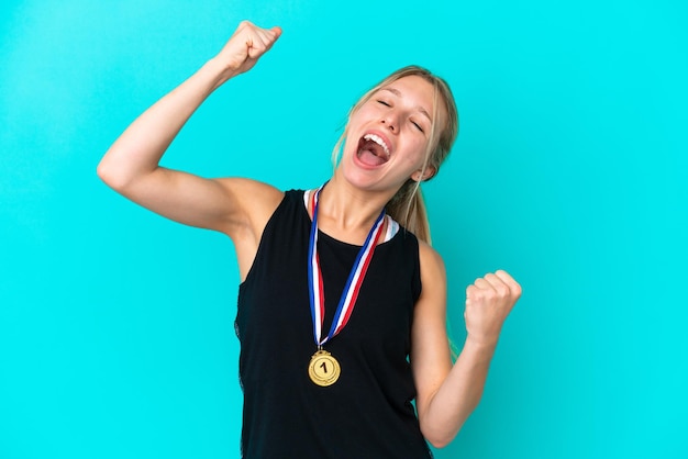 Foto joven caucásica con medallas aisladas de fondo azul celebrando una victoria