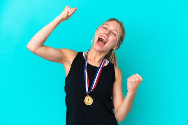 Joven caucásica con medallas aisladas de fondo azul celebrando una victoria