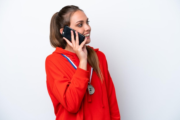 Foto joven caucásica con medallas aisladas de fondo blanco manteniendo una conversación con alguien por teléfono móvil