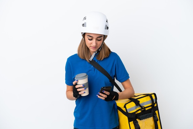 Joven caucásica con mochila térmica aislada de fondo blanco sosteniendo café para llevar y un móvil