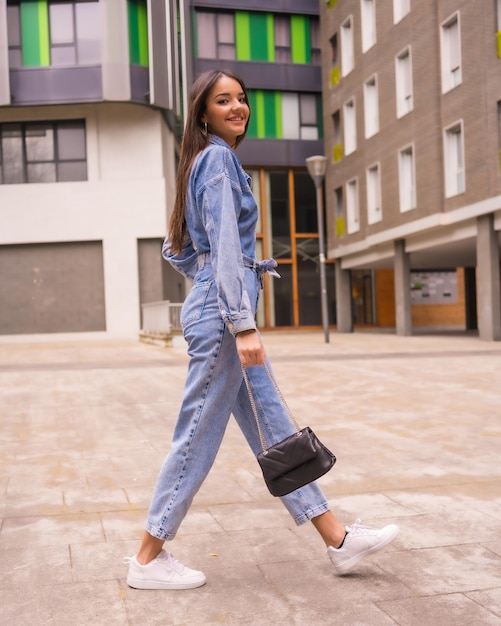 Joven caucásica con un mono vaquero y una bolsa negra Disfrutando de la ciudad en el estilo de vida de vacaciones de una joven caminando algunas fotos urbanas de la casa verde fotos verticales