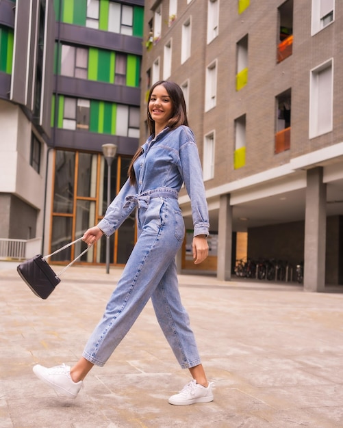 Joven caucásica con un mono vaquero y una bolsa negra Disfrutando de la ciudad en el estilo de vida de vacaciones de una joven caminando algunas fotos urbanas de la casa verde fotos verticales