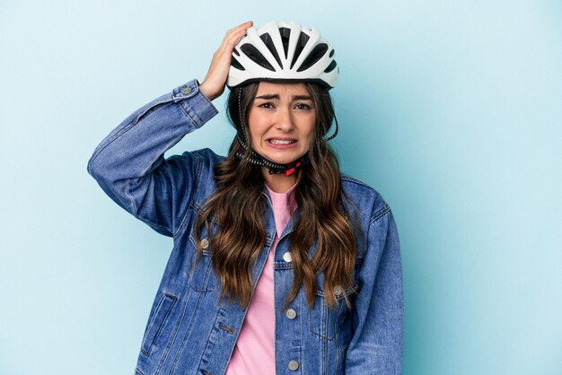 Una joven caucásica montando una bicicleta aislada de fondo azul sorprendida de haber recordado una reunión importante