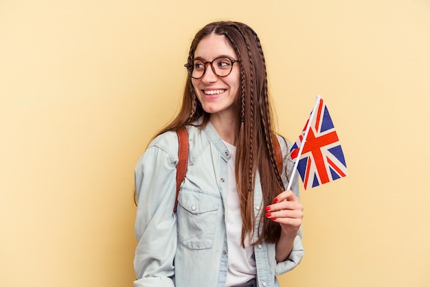 Una joven caucásica que estudia inglés aislada de fondo amarillo parece sonriente, alegre y agradable.