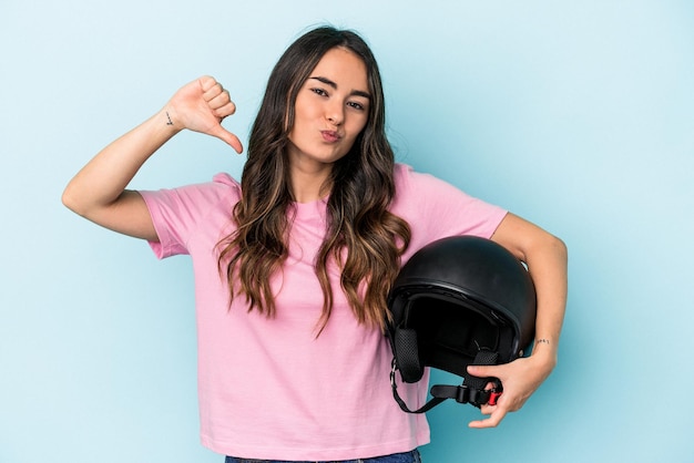 Una joven caucásica que sostiene un casco de moto aislado en un fondo azul se siente orgullosa y segura de sí misma como ejemplo a seguir