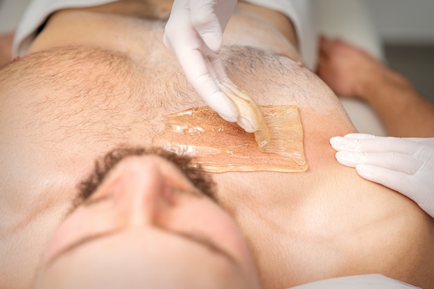 Joven caucásica recibiendo depilación de su pecho en un salón de belleza depilación mens torso