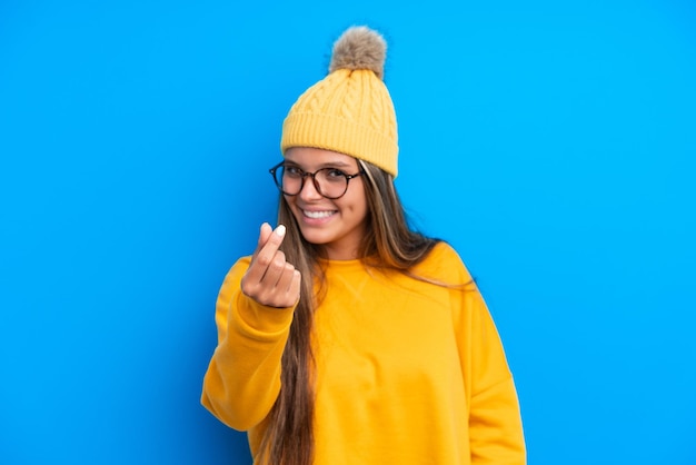 Joven caucásica con ropa de invierno aislada de fondo azul haciendo gestos de dinero