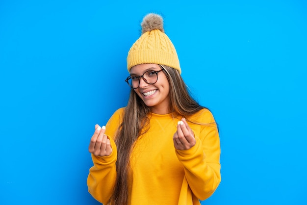 Joven caucásica con ropa de invierno aislada de fondo azul haciendo gestos de dinero