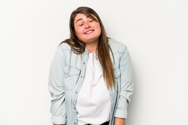 Una joven caucásica con sobrepeso aislada de fondo blanco se ríe y cierra los ojos, se siente relajada y feliz.