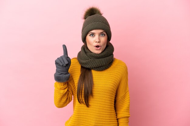 Joven caucásica con sombrero de invierno aislado en la pared rosa con la intención de darse cuenta de la solución mientras levanta un dedo