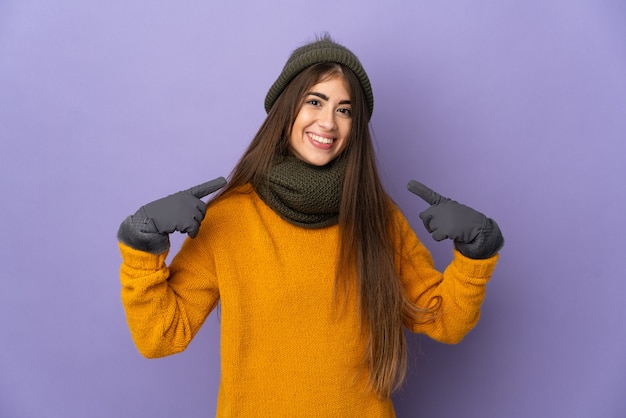 Joven caucásica con sombrero de invierno aislado sobre fondo púrpura dando un pulgar hacia arriba gesto