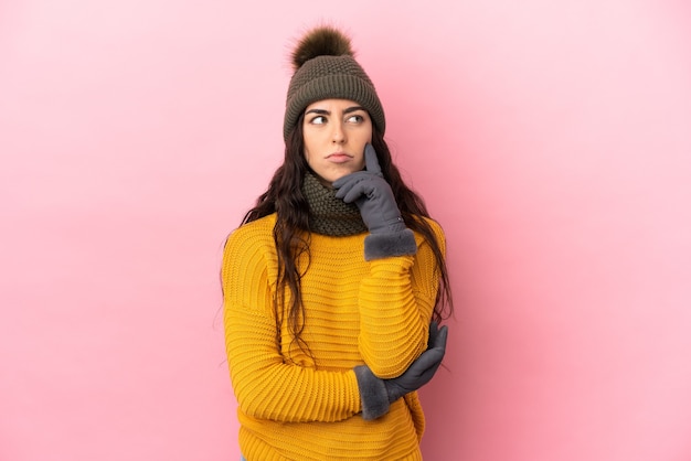 Joven caucásica con sombrero de invierno aislado sobre fondo púrpura con dudas mientras mira hacia arriba