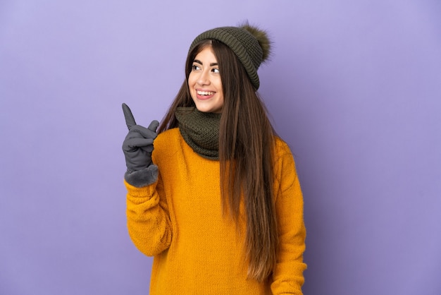 Joven caucásica con sombrero de invierno aislado sobre fondo púrpura con la intención de darse cuenta de la solución mientras levanta un dedo