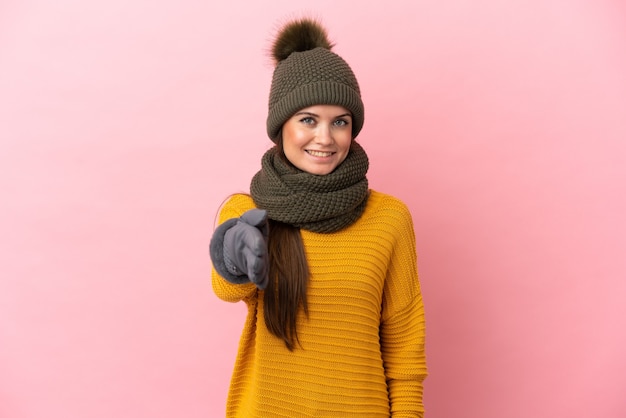 Joven caucásica con sombrero de invierno aislado sobre fondo rosa estrecharme la mano para cerrar un buen trato